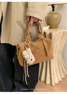 Detail of caramel brown leather handbag with gold logo and plush puppy charm