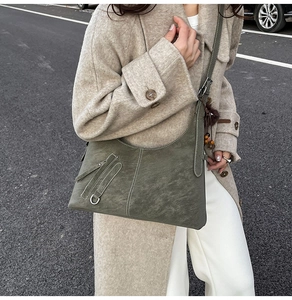 Detail of dark green shoulder bag with white contrast stitching and decorative pompom