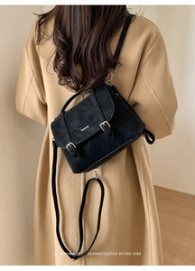 Minimalist black vintage messenger bag with dual buckles and slim shoulder strap worn on coat