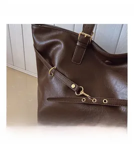 Dettaglio della pelle martellata e hardware dorato su borsa tote marrone scuro