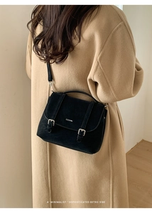 Detail of a vintage black crossbody bag with silver buckles on a khaki coat model