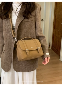 Close-up of retro brown leather crossbody bag with silver buckles on a tweed coat