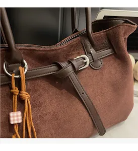 Detail of dark brown suede tote with silver hardware buckle and decorative beaded charm
