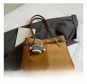 Détail du cabas en daim caramel avec coutures, sangles en cuir et pendentif d'ours