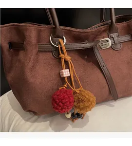 Detail of dark brown suede tote bag featuring colorful pompom charms and silver hardware