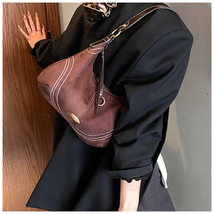 Macro view of dark brown suede bag featuring white contrast stitching and gold logo