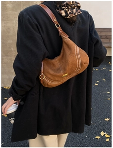 Close-up of brown suede crescent bag with white contrast stitching and gold hardware