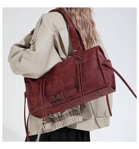 Detail view of burgundy leather tote bag featuring fringe tassels and metal rivet studs