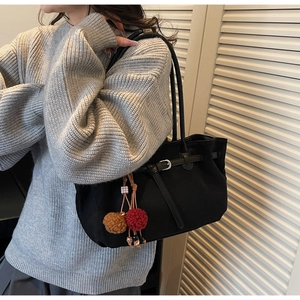 Close-up of black tote bag with leather drawstring detail and decorative plush charms