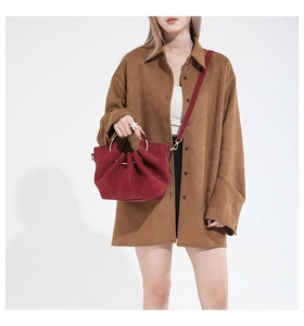 Detail view of red suede handbag with ruffle design and metallic handle worn by a model