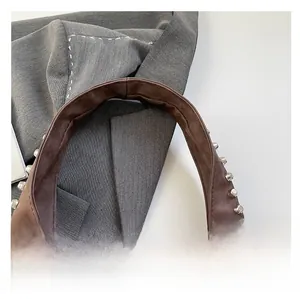 Detailed macro view of brown suede tote bag strap featuring silver metal rivet studs