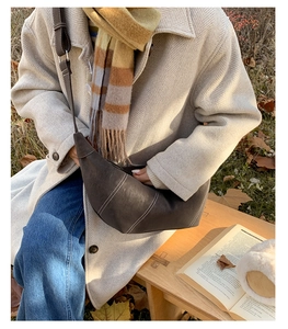 Detail of dark brown crescent bag with white stitching shown in outdoor lifestyle setting