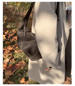 Detail of a dark brown crescent bag with white contrast stitching and adjustable strap