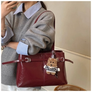 Dettaglio della borsa tote in pelle bordeaux con trama retrò e ciondolo a forma di orsetto