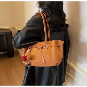 Brown suede tote bag detail with decorative fur pompom and slender leather buckle charm