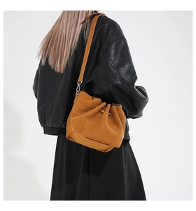 Detail of adjustable strap and drawstring design on the tan leather bucket shoulder bag
