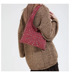Détail d'un sac à bandoulière en daim bordeaux avec clous argentés et forme atypique