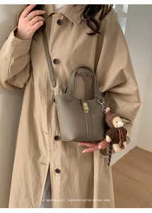 Détail d'un sac seau gris en cuir grainé avec boucle dorée et pendentif ours en peluche