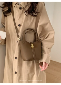 Détail d'un sac seau en cuir marron avec fermoir doré porté sur un trench-coat beige