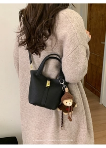 Detail of black lychee grain bucket bag with gold lock and a brown knit bear charm