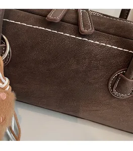 Detailed view of brown leather bag featuring contrast stitching and plush pompom accessory