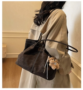 Detail view of large brown suede tote bag with white contrast stitching and plush bear charm