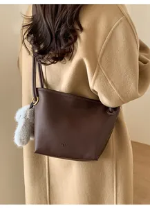 Detail of dark brown pebble leather bucket bag with plush rabbit charm on a camel coat