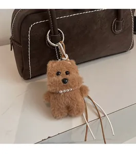 Brown fluffy bear keychain charm with pearl necklace and metal tag on leather bag