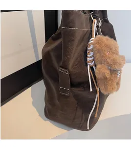 Detail of dark brown tote bag with white stitching and plush bear charm accent