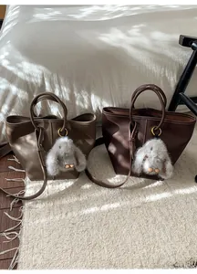 Close-up of litchi grain leather tote bags with plush rabbit charm and metal ring detail