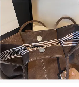 Detail of dark brown tote bag showing magnetic silver closure and striped fabric lining