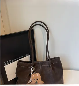 Detail of dark brown tote bag featuring white contrast stitching and plush bear charm