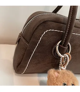 Detail of dark brown suede bag featuring bold white stitching and a plush bear charm