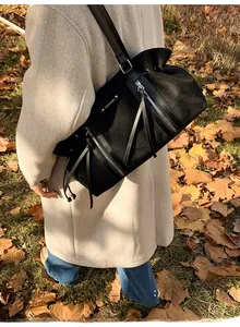 Black matte leather tote bag with silver logo detail shown in an outdoor autumn setting