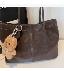 Detail of dark brown tote bag with white stitching and cute plush dog charm