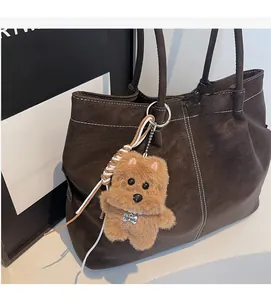 Plush brown dog charm with metal collar on leather tote bag handle detail