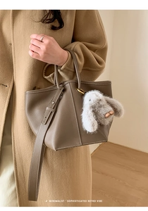 Close-up of ivory leather bucket bag with white contrast stitching and plush bunny charm
