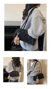 Detail of black matte underarm bag with white stitching and cute brown puppy plush charm