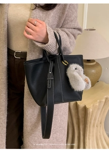 Detail of black pebbled leather tote with white stitching and grey plush bunny charm