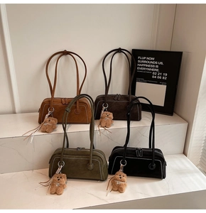 Detail of suede shoulder bags in four colors with teddy bear pendants on marble steps