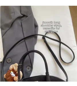 Detail einer schwarzen Wildleder-Hobo-Tasche mit glattem Schultergurt und süßem Anhänger