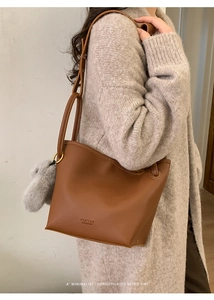 Close-up of brown pebbled leather bucket bag with FAY'TOR logo and grey pompom charm