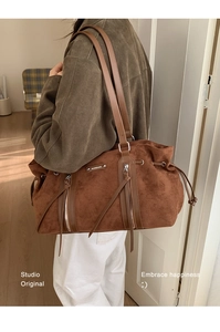 Close-up of brown suede shoulder bag featuring dual shoulder straps and metal logo detail