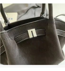 Detailansicht der dunklen Lederstruktur und silbernen Metallschließe an der Handtasche
