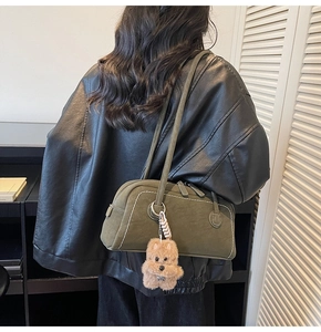 Detail of green Boston bag with white stitching and a cute teddy bear charm