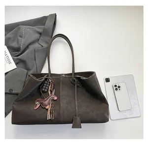 Nahaufnahme der dunkelbraunen Retro-Leder-Tote mit Hund-Anhänger auf grauem Anzug