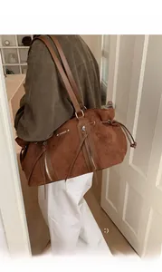 Detail of caramel brown suede tote bag with slim leather straps and metal logo plate