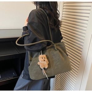 Detail view of large olive green suede tote bag with contrast stitching and bear charm