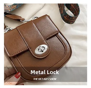 Close-up of vintage brown saddle bag featuring a silver oval twist lock and printed strap