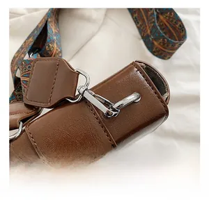 Close-up of shiny metal swivel hook and ethnic printed strap on dark brown saddle bag